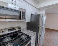 Modern kitchen at Huntley Ridge East featuring stainless steel appliances, including a microwave, refrigerator, and stove with smooth countertops and white cabinetry.