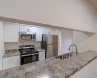 Spacious renovated kitchen at Huntley Ridge East with stainless steel appliances, white cabinets, granite-style countertops, and a breakfast bar overlooking the dining area.