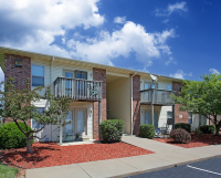 Two-story apartment building with brick and siding exterior, private balconies and patios, and landscaped grounds with trimmed shrubs, trees, and mulch beds